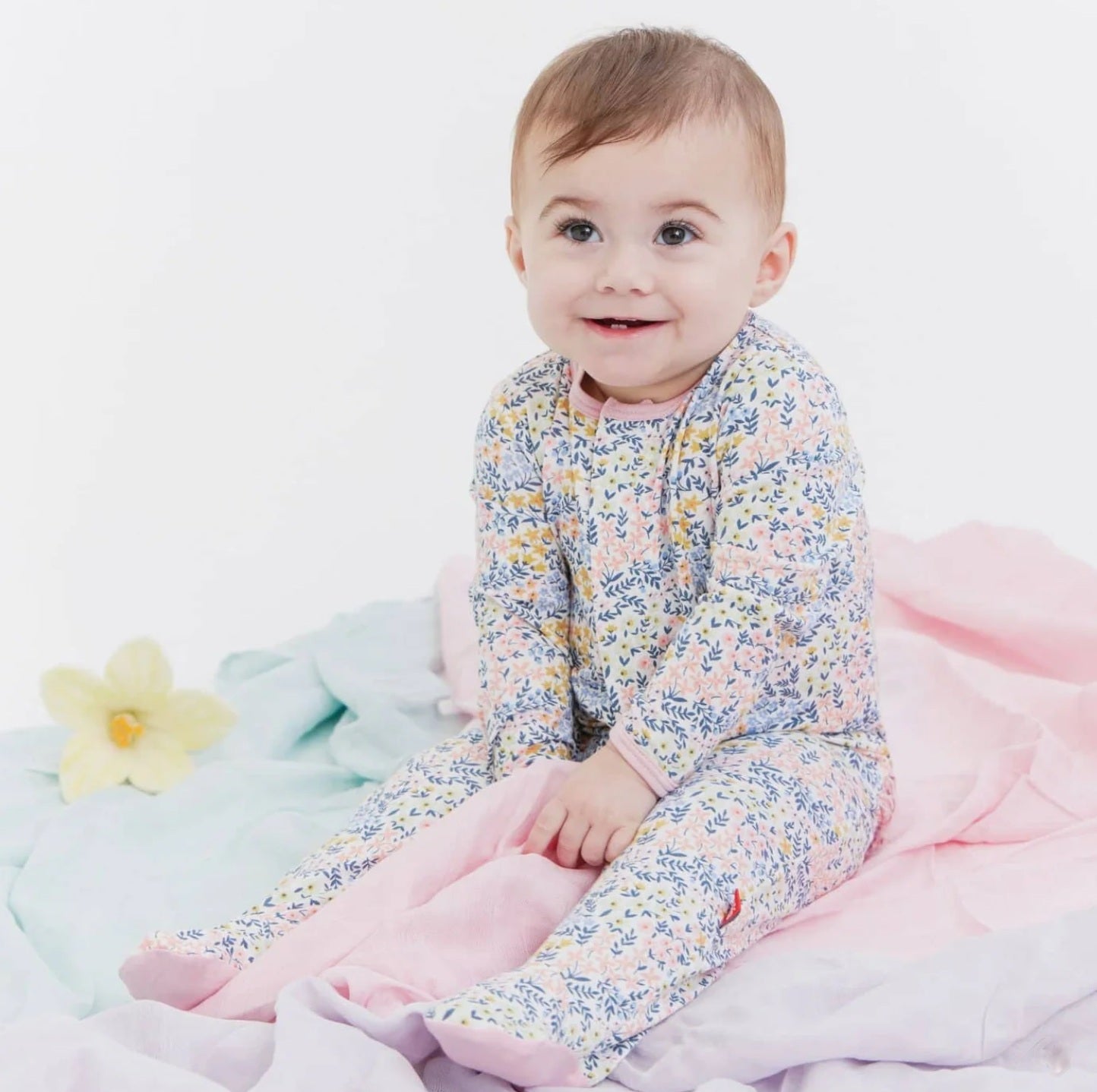 Baby in a floral outfit sitting on a soft surface with a white background