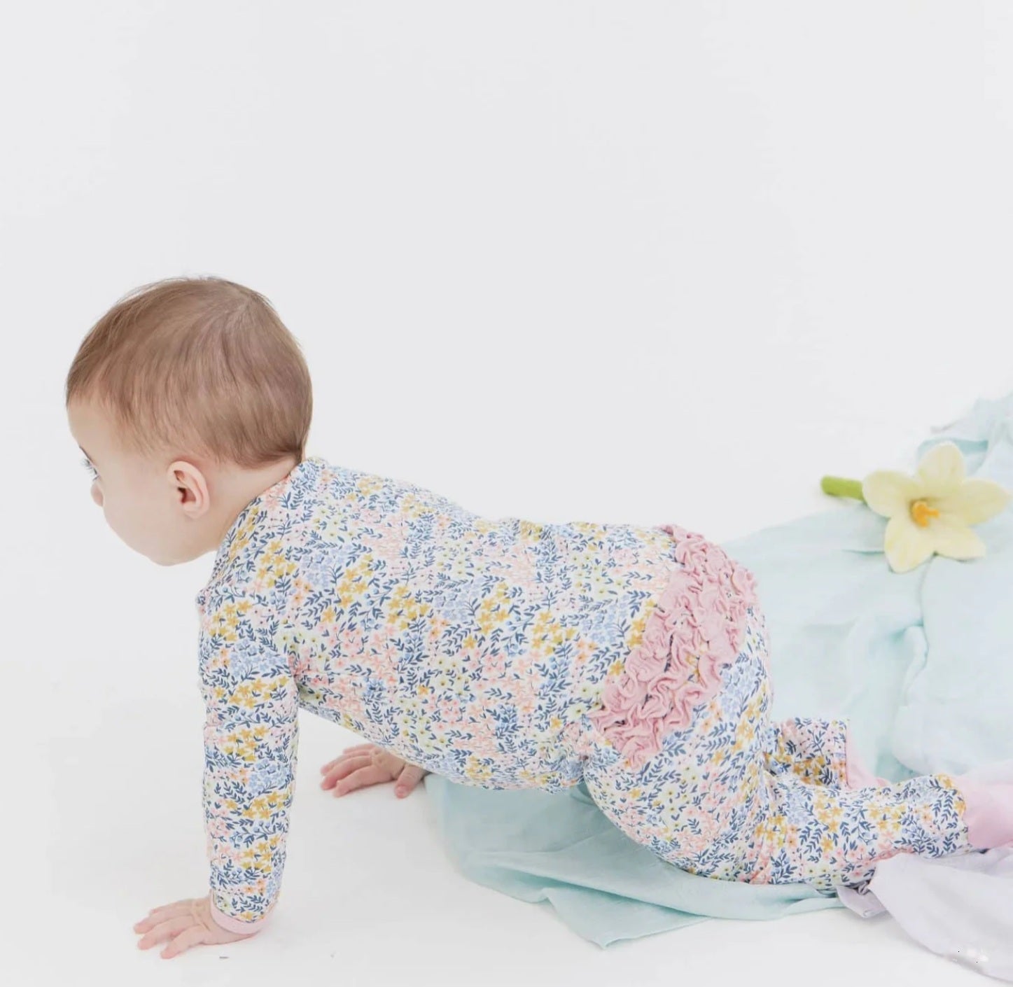 Baby in a floral onesie crawling on a white surface with flowers in the background