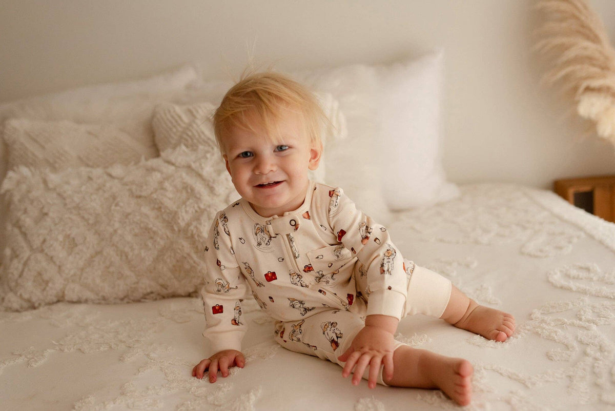 Baby sitting on a bed wearing a Paddington bear long sleeve romper.
