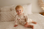 Baby sitting on a bed wearing a Paddington bear long sleeve romper.