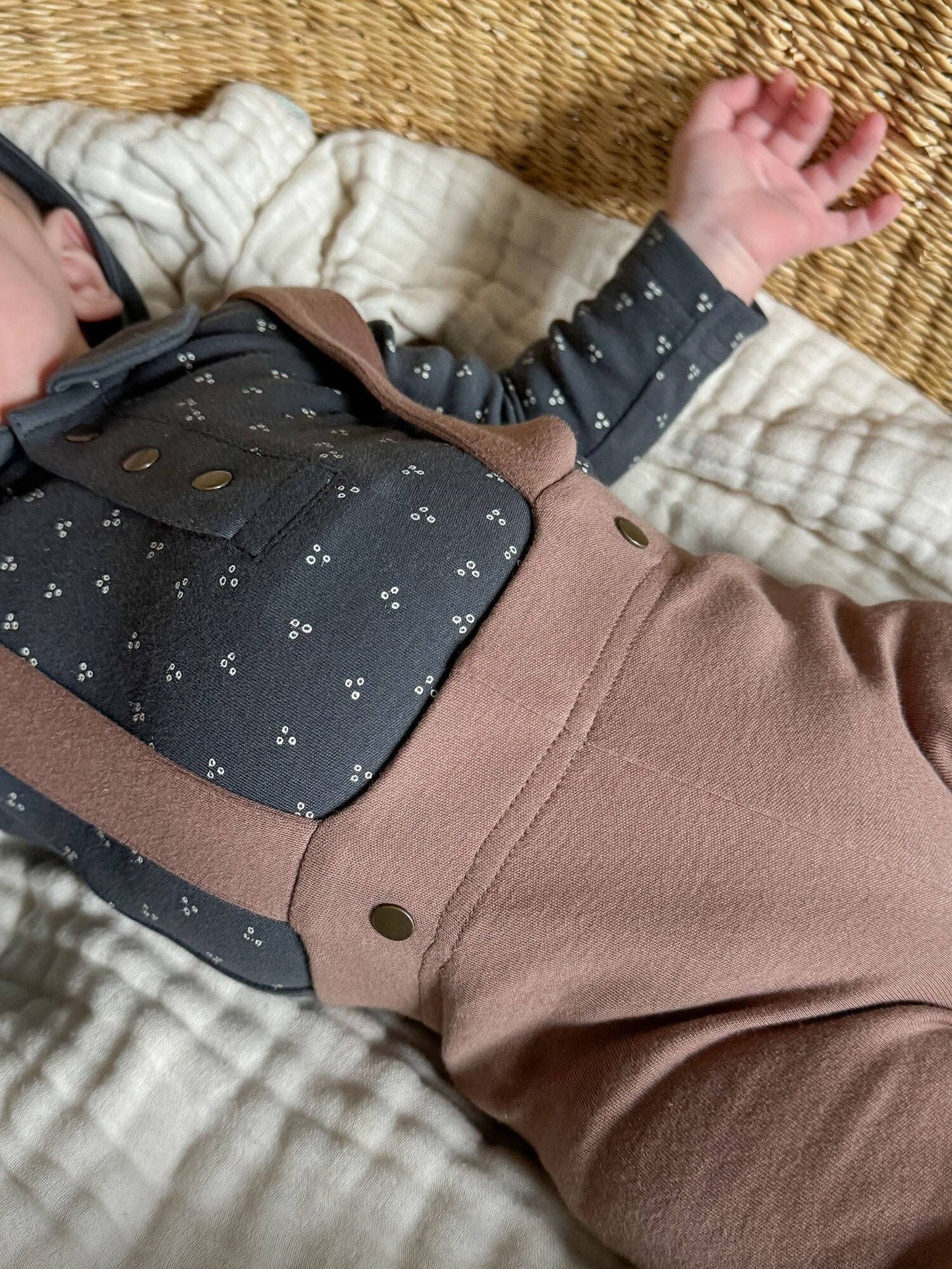 Close-up of a baby wearing brown pants with suspenders laying on a textured surface
