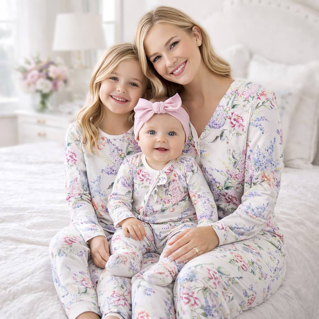 Woman and two children in matching floral pajamas sitting on a bed.