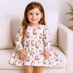 Young girl wearing a dress with fox pattern sitting on a white couch.