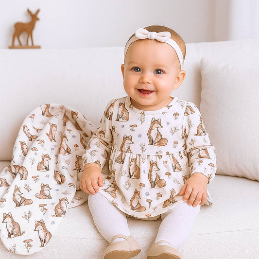 Baby sitting on a couch wearing a fox-patterned outfit with a matching blanket.