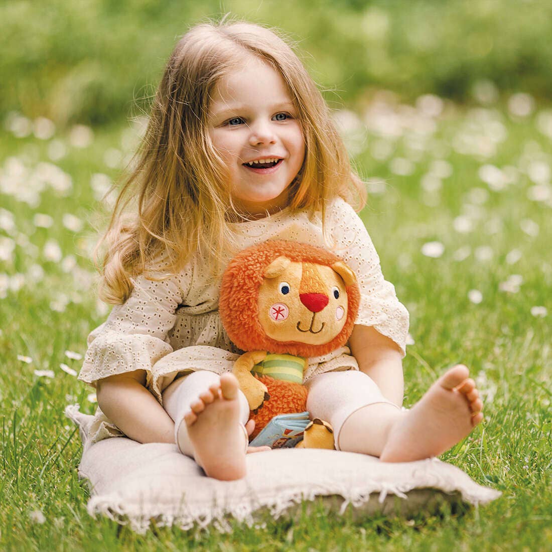 Child sitting on a blanket in a grassy field holding Bababoo plush toy.