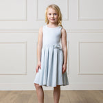 Young girl wearing a light blue dress against a white paneled wall.