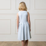 Back of girl wearing a light blue dress against a white paneled wall.