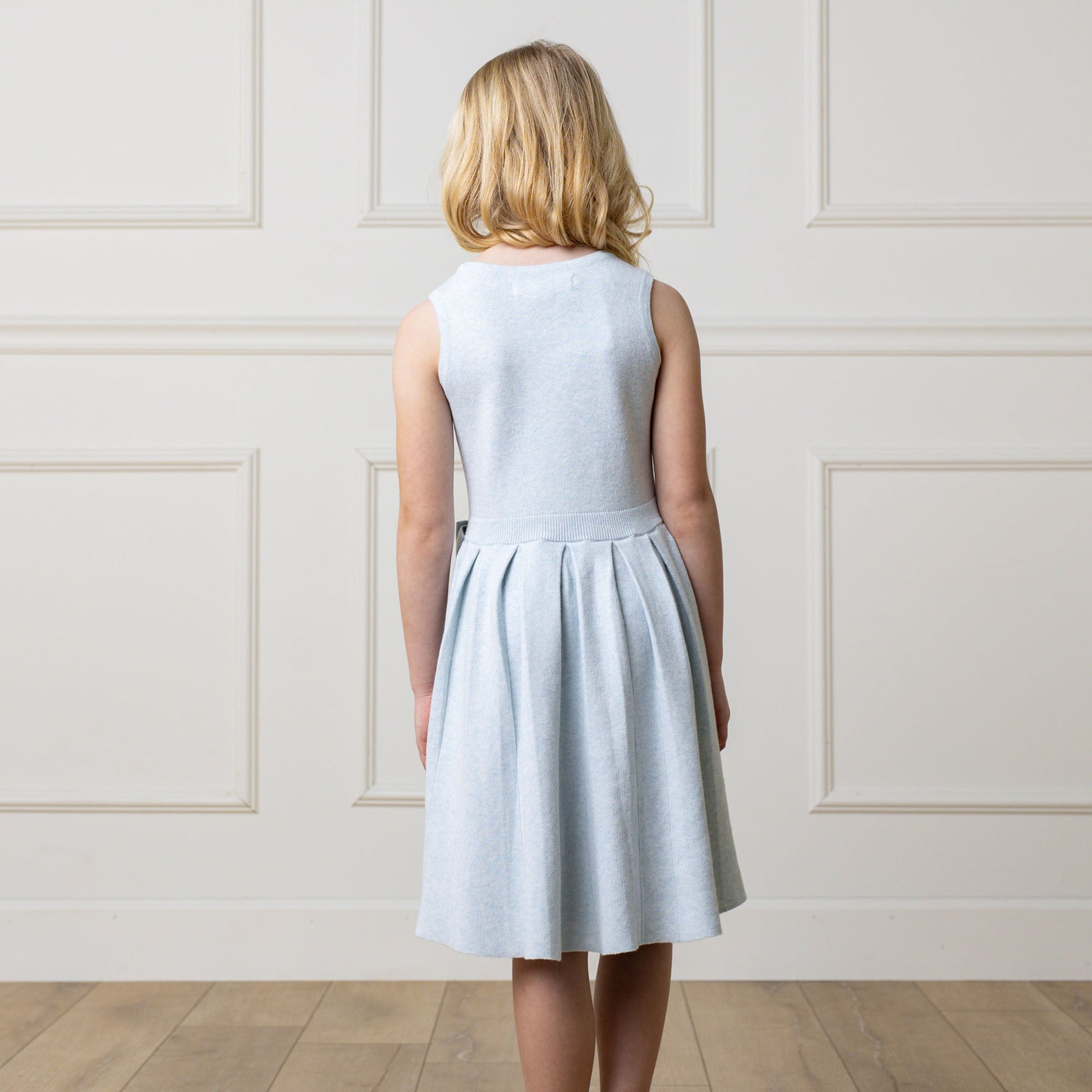 Back of girl wearing a light blue dress against a white paneled wall.