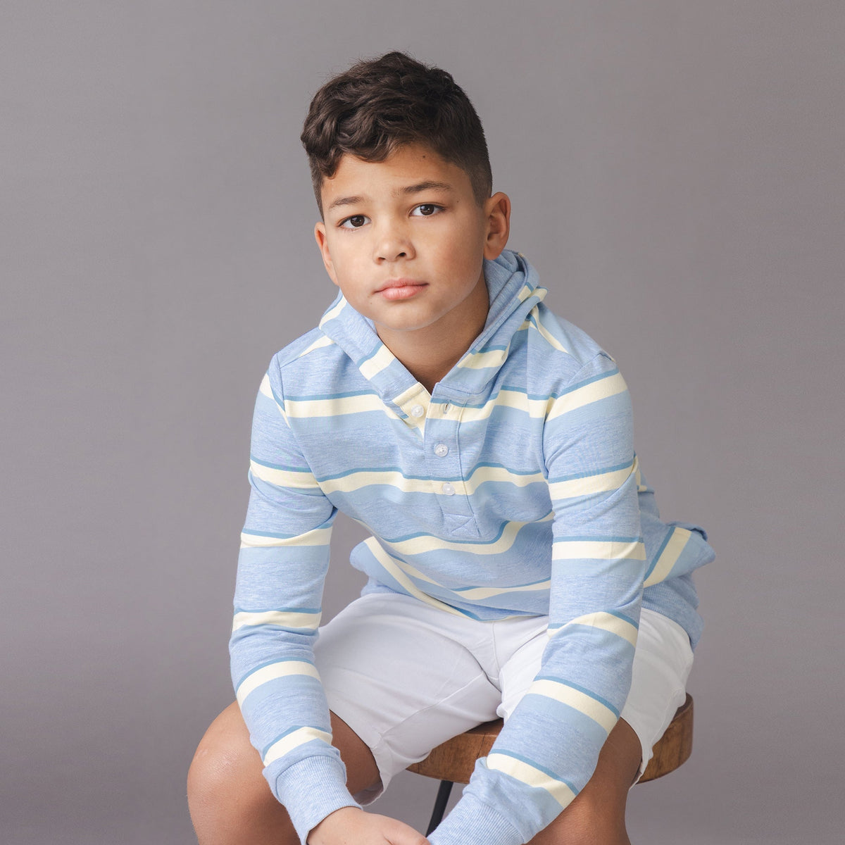 Child wearing a blue and yellow striped shirt sitting on a chair against a gray background