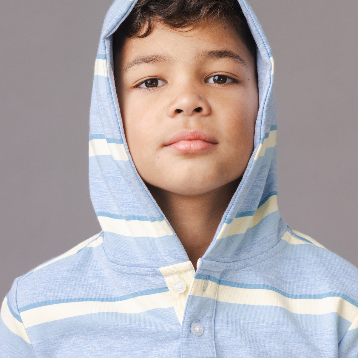Child wearing a blue and yellow striped hoodie against a gray background