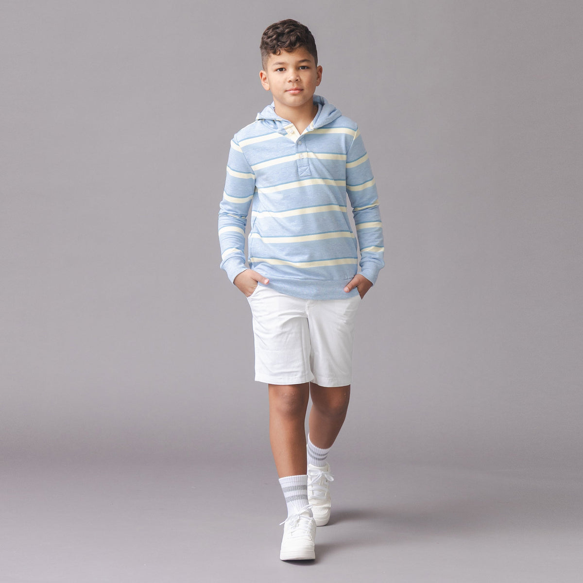 Child wearing a striped hoodie and white shorts on a gray background