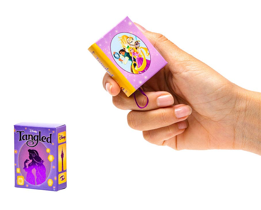 Hand holding a tiny book Tangled with Disney packaging on a white background