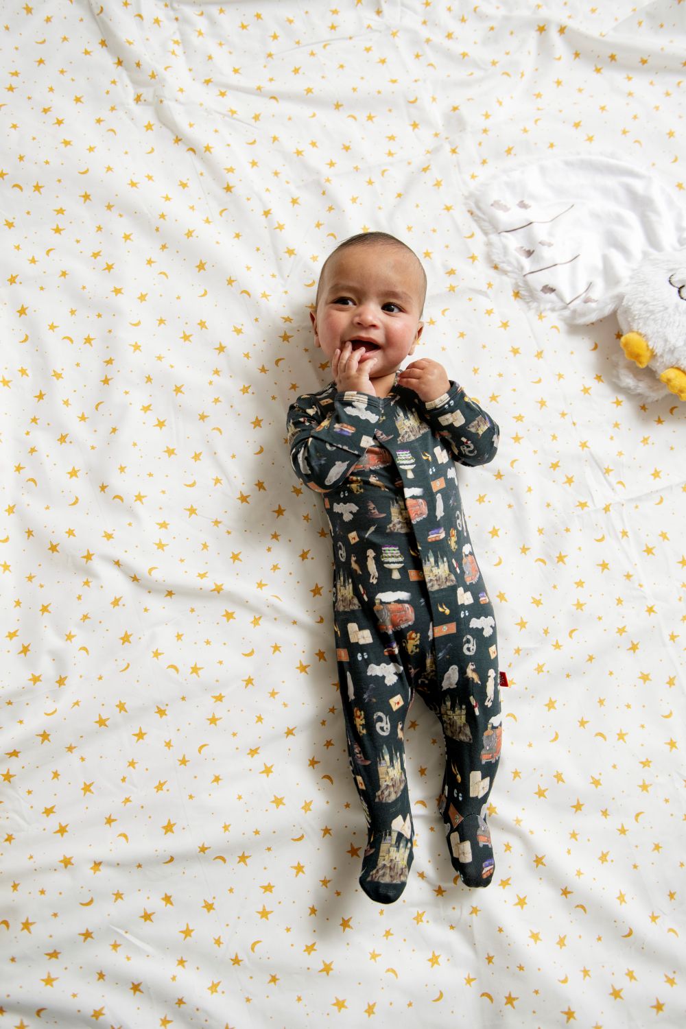 Baby wearing Harry Potter coverall lying on a white blanket with yellow star patterns