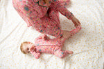 mom and baby in matching pink pajamas on a white bed with yellow dots.