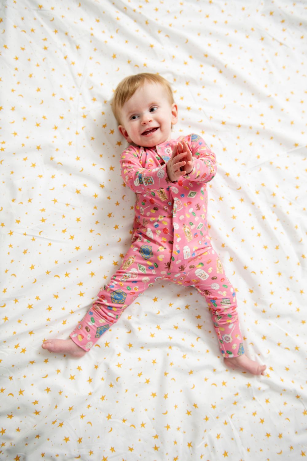 Baby in pink pajamas lying on a white blanket with yellow stars