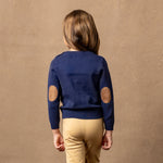 Child wearing a blue sweater with elbow patches on a brown background
