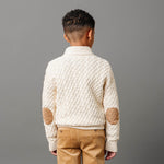 Child wearing a cream knitted sweater with brown elbow patches on a gray background