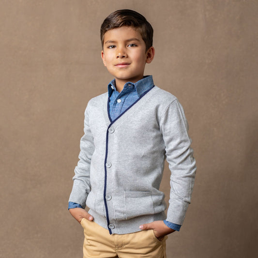 Young boy wearing a gray cardigan with blue trim over a blue shirt, standing against a brown background.