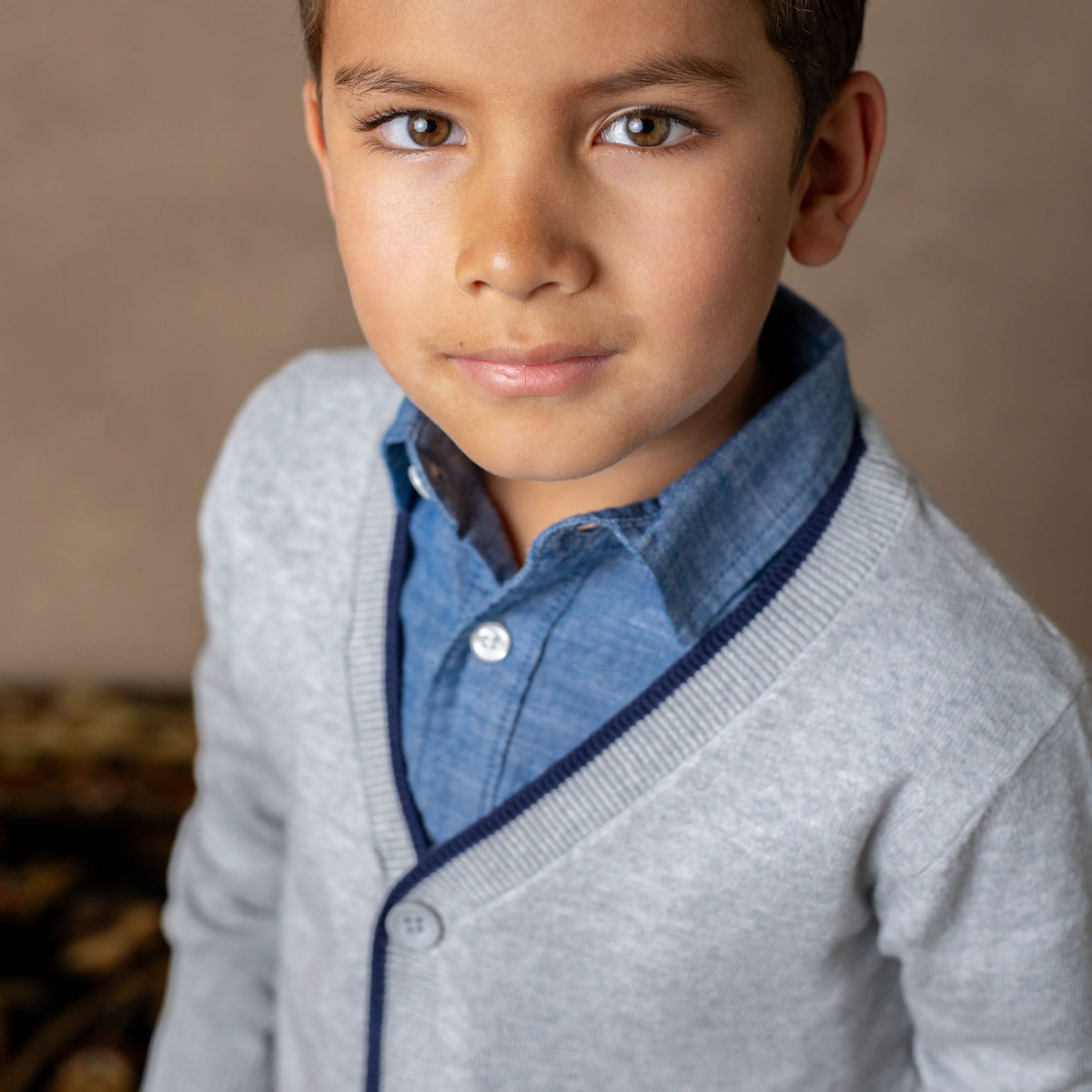 Young boy wearing a gray sweater over a blue shirt against a neutral background
