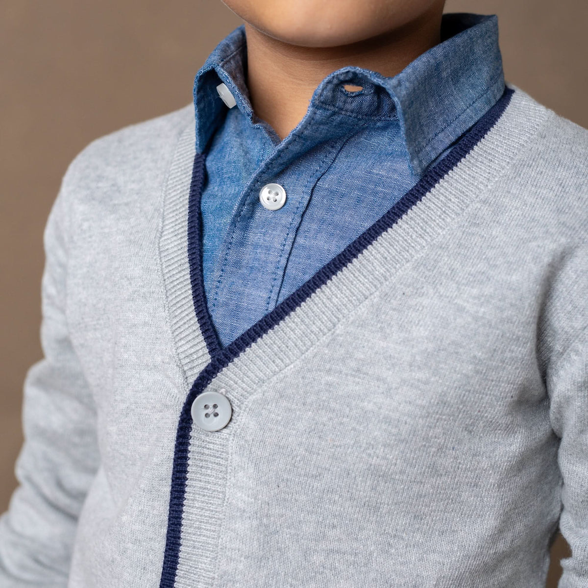Person wearing a gray sweater over a blue shirt with a brown background