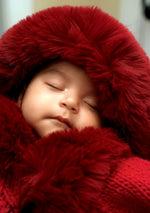 A close-up of a sleeping baby wrapped in a bright red fuzzy hooded outfit, with the face mostly covered by the plush red fabric.