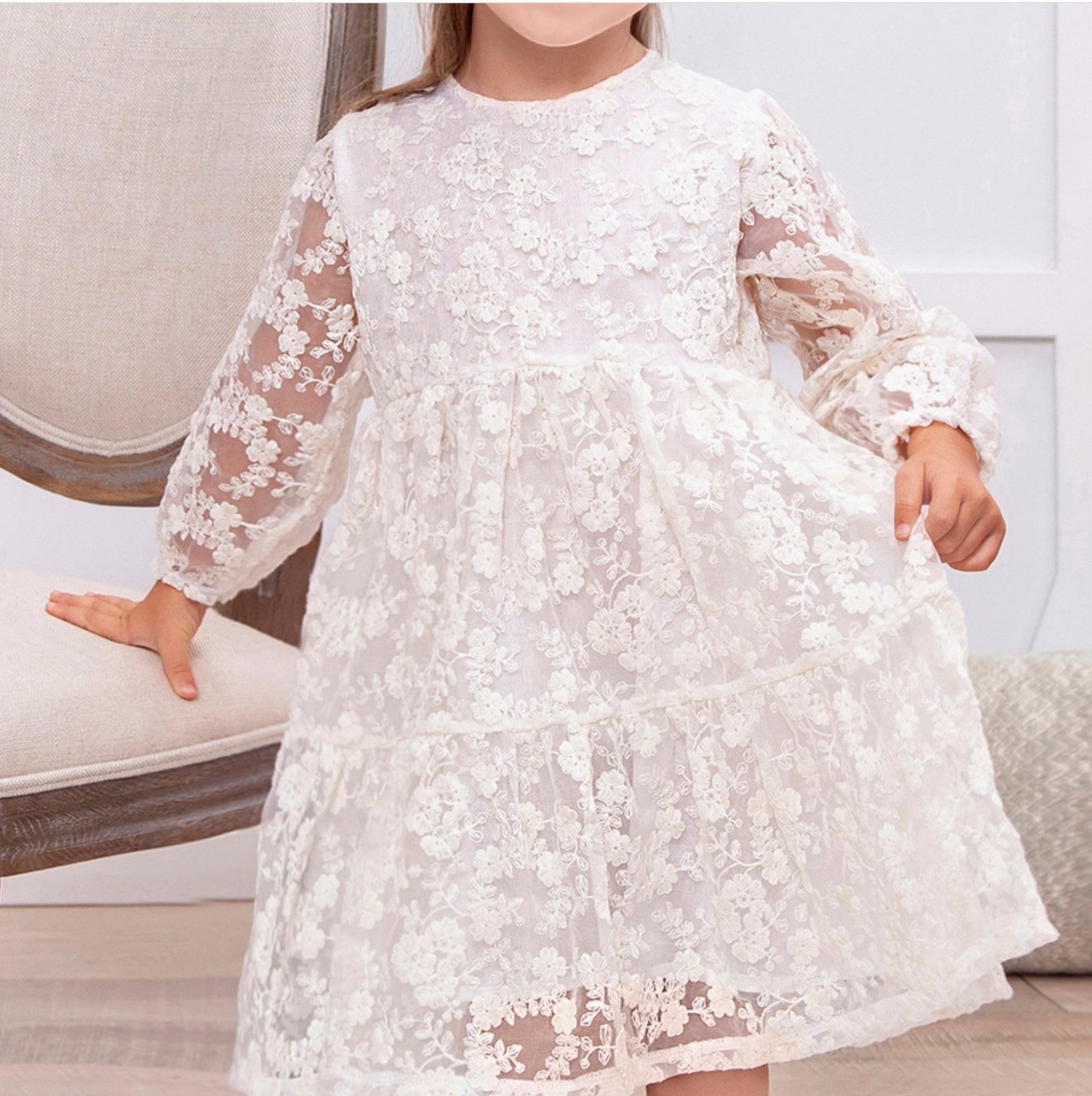 Child wearing a white lace dress sitting on a couch.
