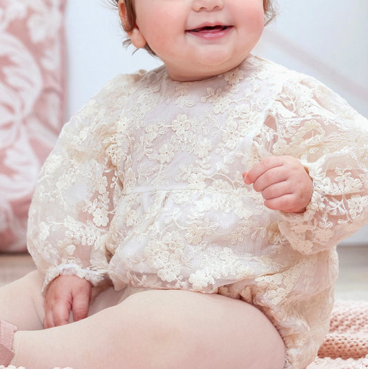 Baby wearing a lace outfit sitting on a soft surface