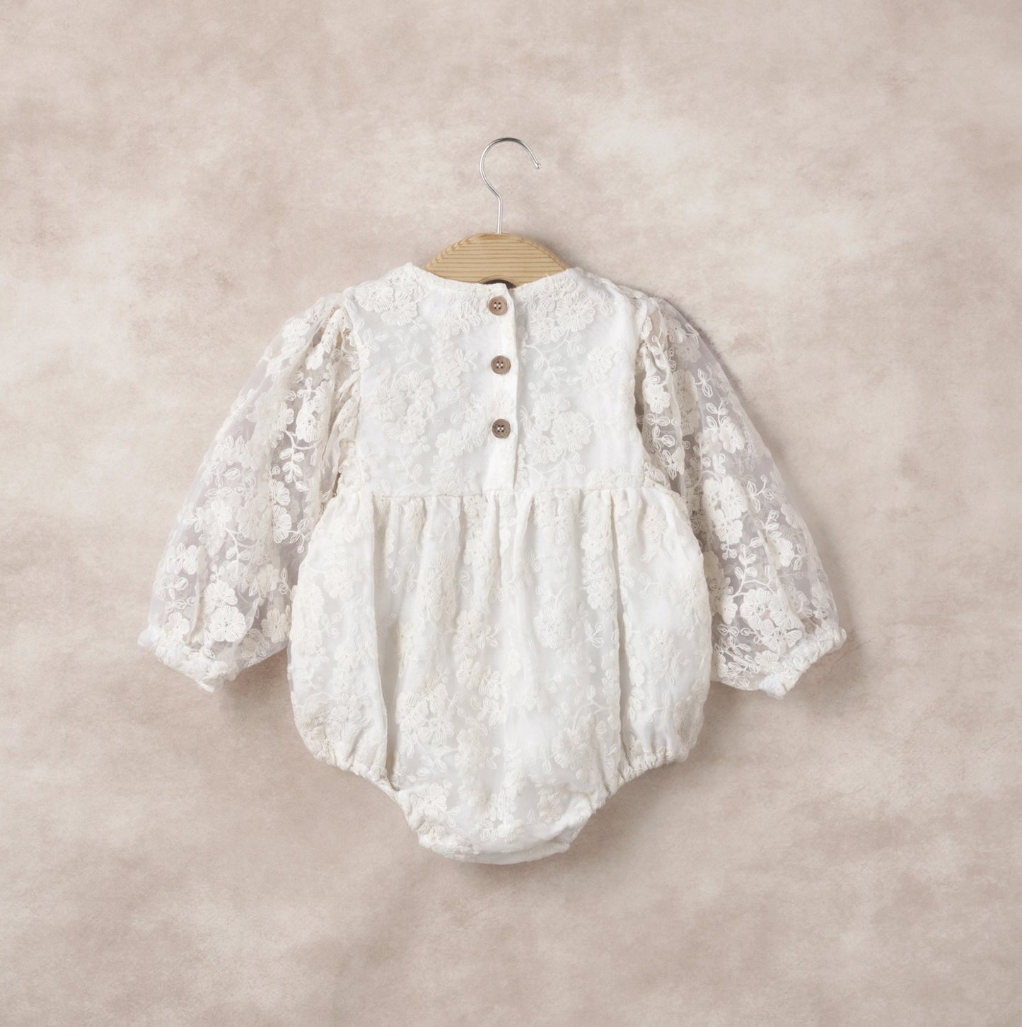 White lace baby romper on a hanger against a beige background