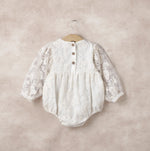 White lace baby romper on a hanger against a beige background