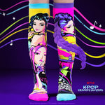 A pair of knee-high socks with vibrant, colorful K-pop character prints, shown on a stylized dark purple background with neon lines and music notes. The socks feature detailed illustrations of characters with braided hair in pink, yellow, purple, and blue.