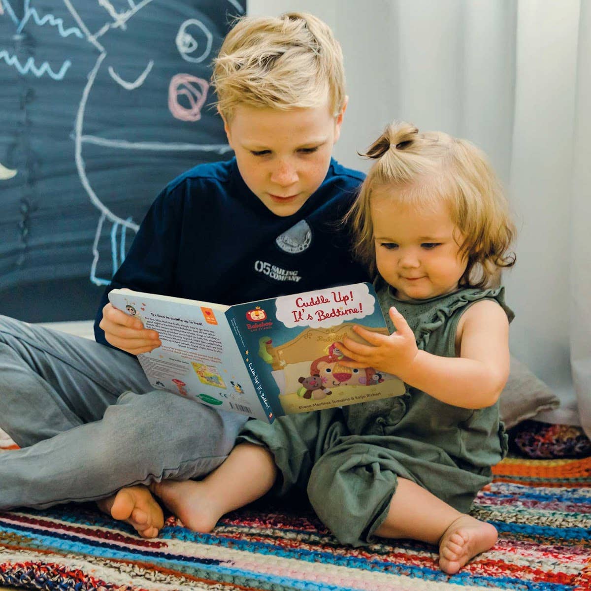 Two children reading a book together on a colorful rug.