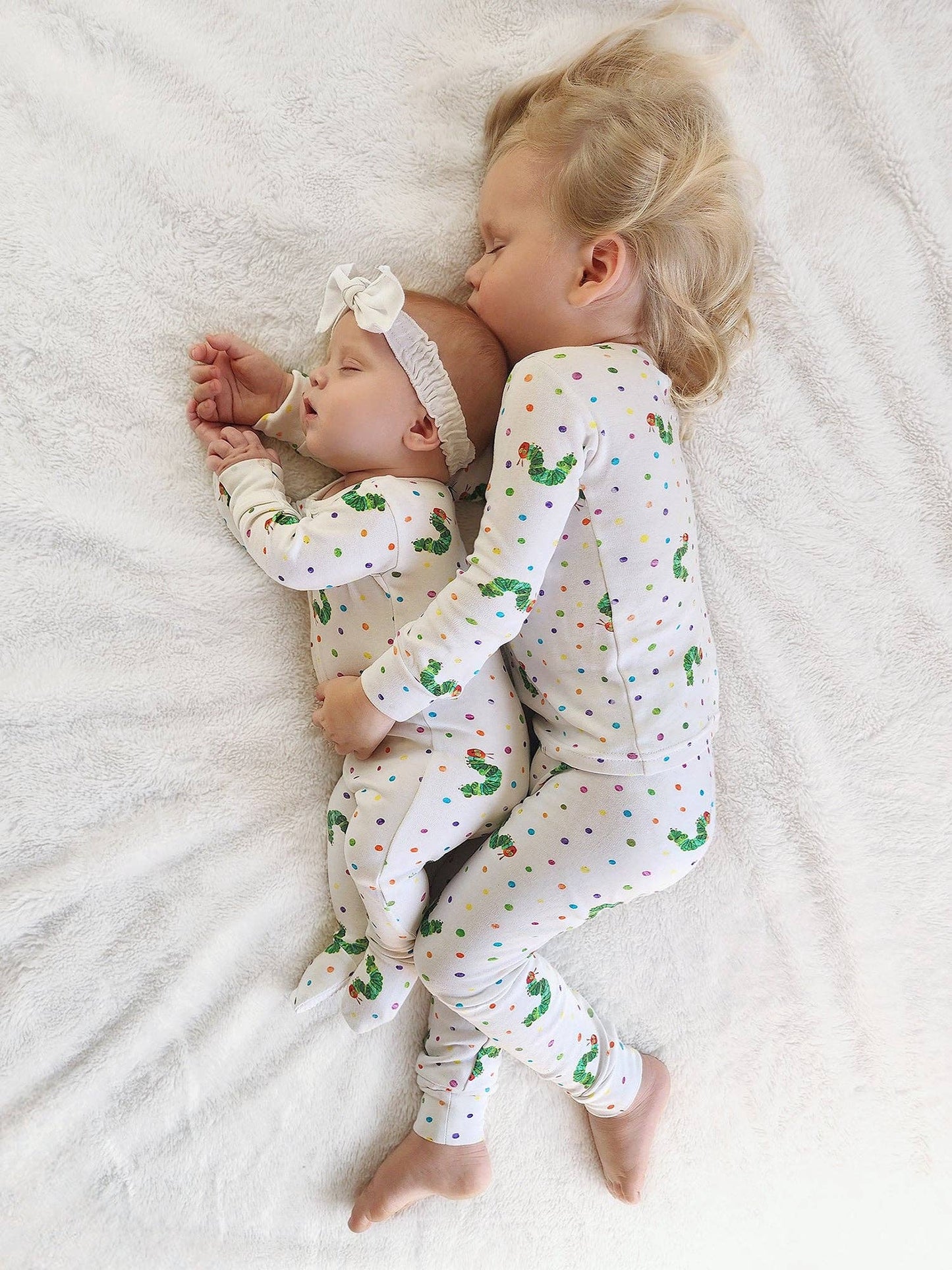Two children wearing matching pajamas with a pattern of green characters on a white blanket.