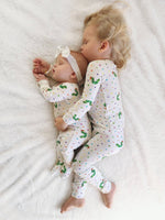 Two children wearing matching pajamas with a pattern of green characters on a white blanket.