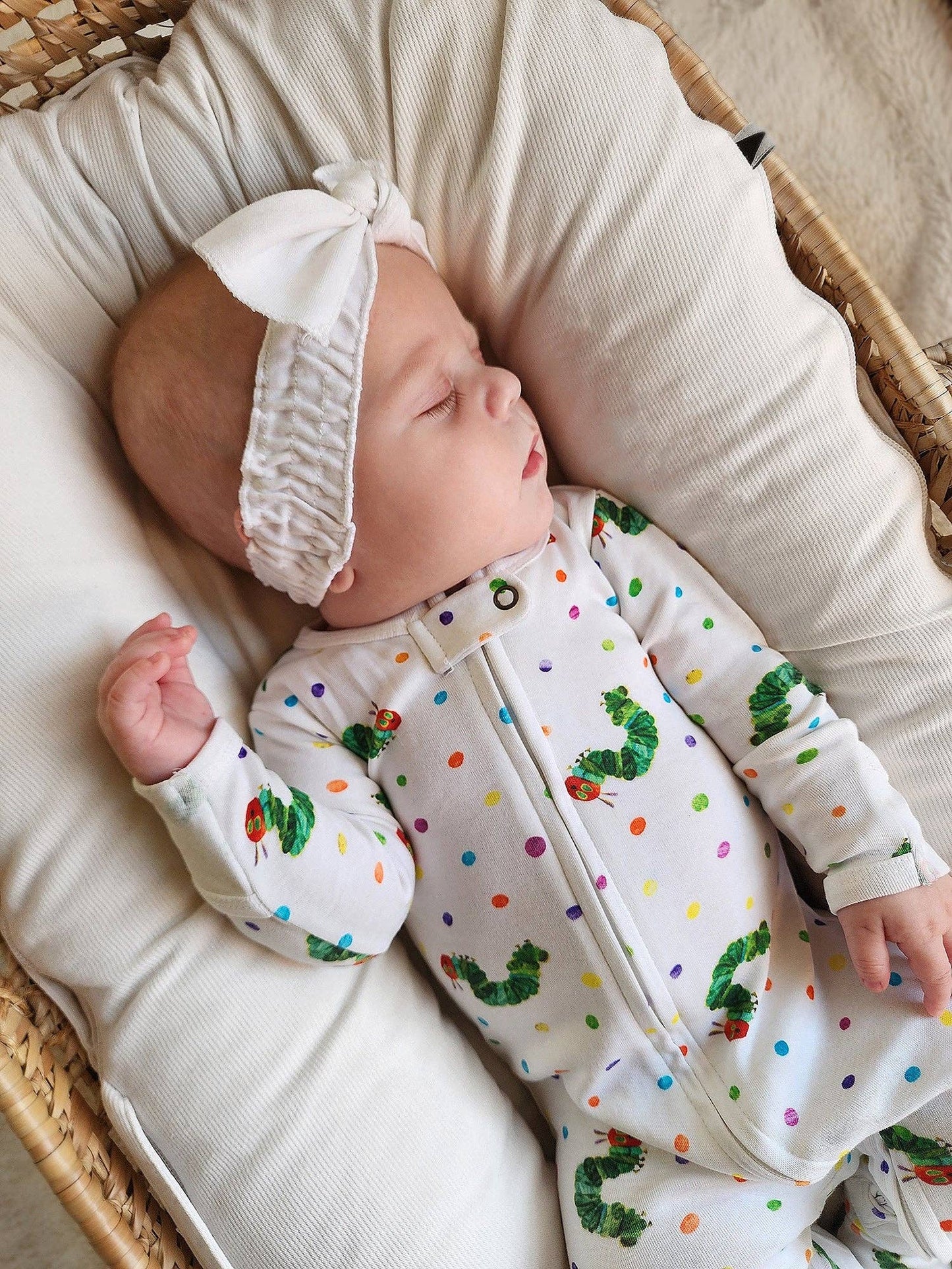 Baby in a polka dot outfit with colorful designs, lying in a crib.