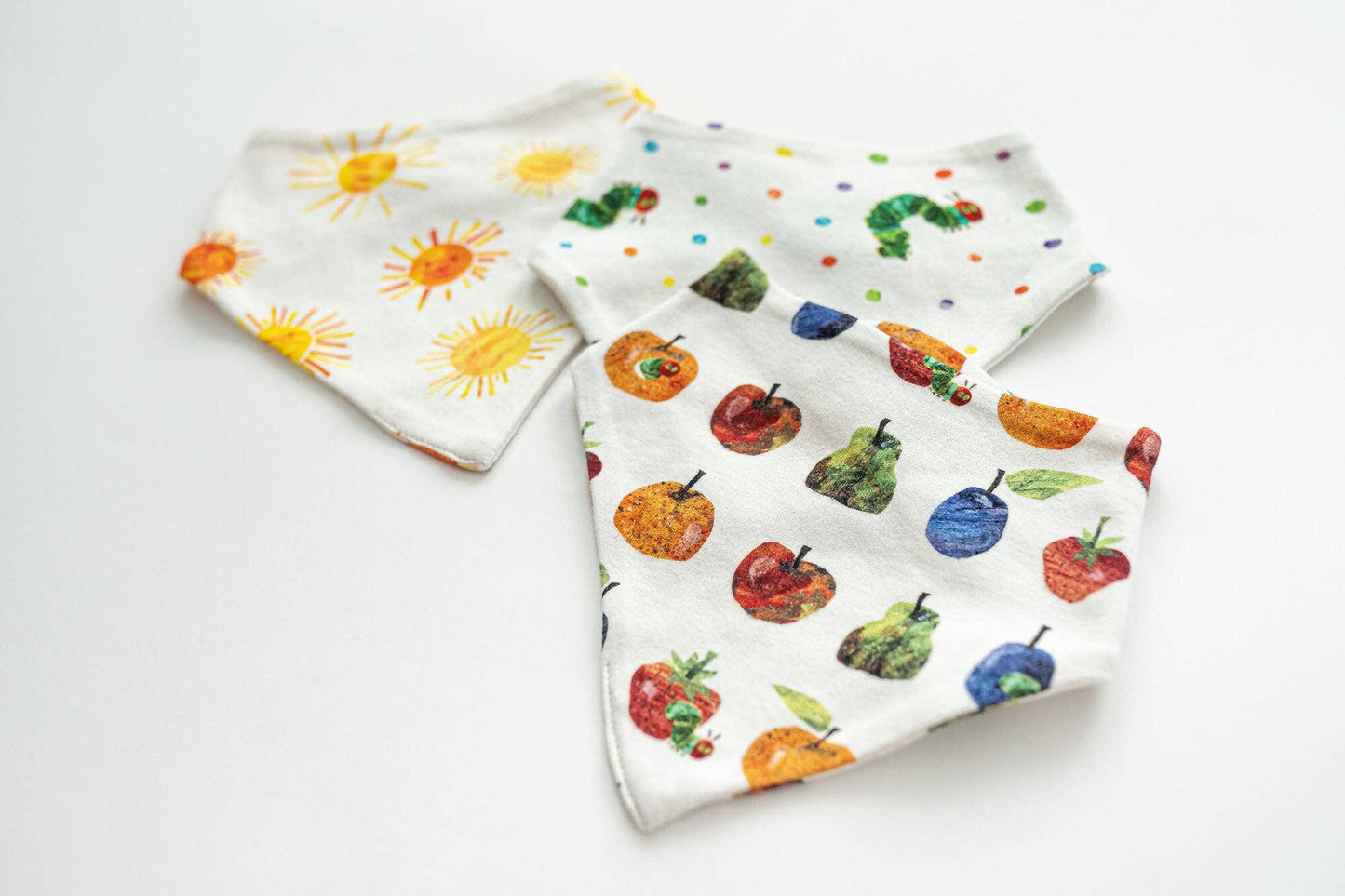 Three baby bibs with colorful fruit, vegetable, and sun patterns on a white background