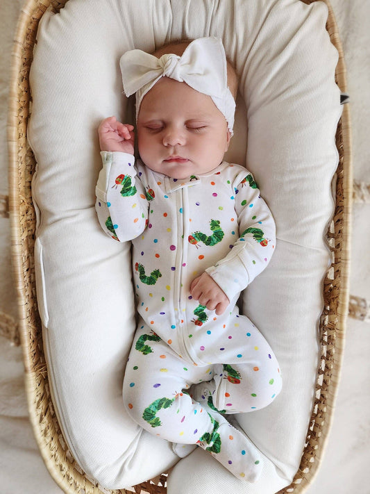 Newborn baby in a white outfit with green caterpillar pattern, lying in a moses basket.