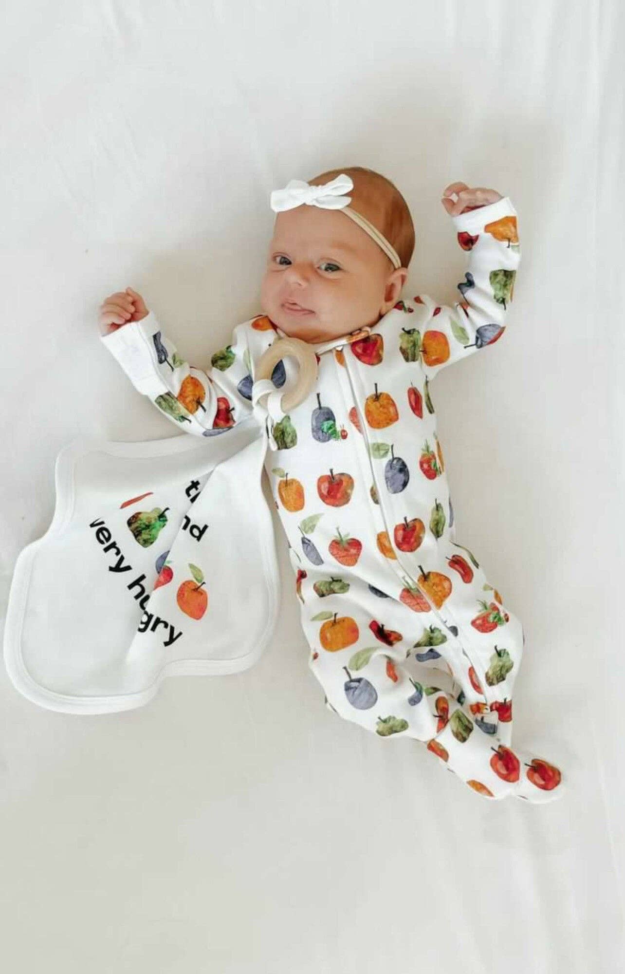 Baby wearing a colorful fruit-patterned onesie with a bib on a white background