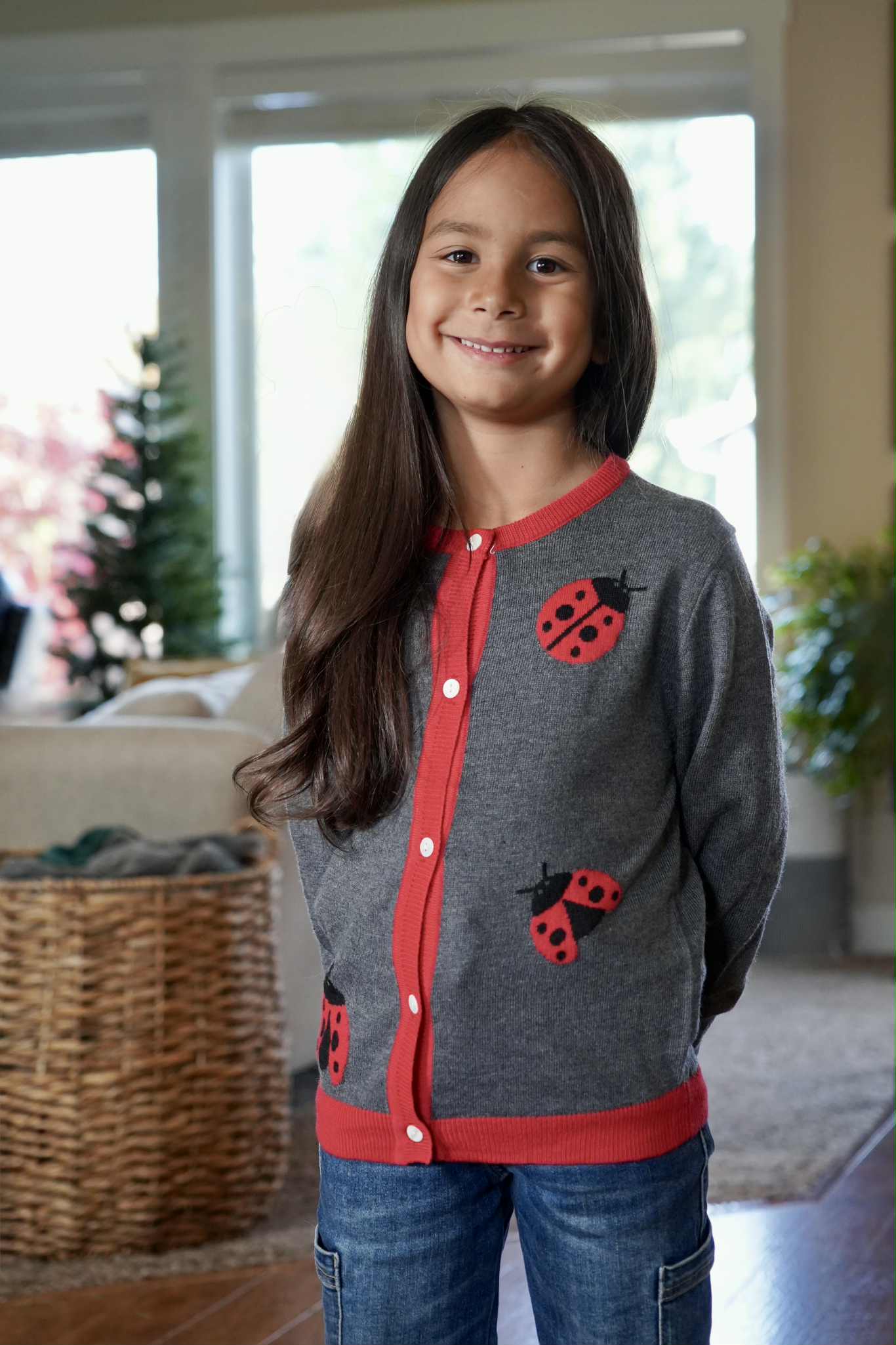 Young girl wearing a gray cardigan with ladybug designs in a home setting