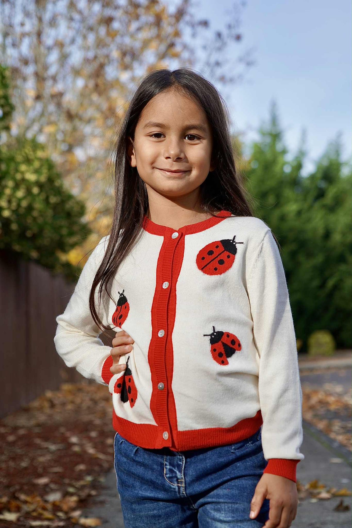 Child wearing a white cardigan with red ladybug patterns outdoors.