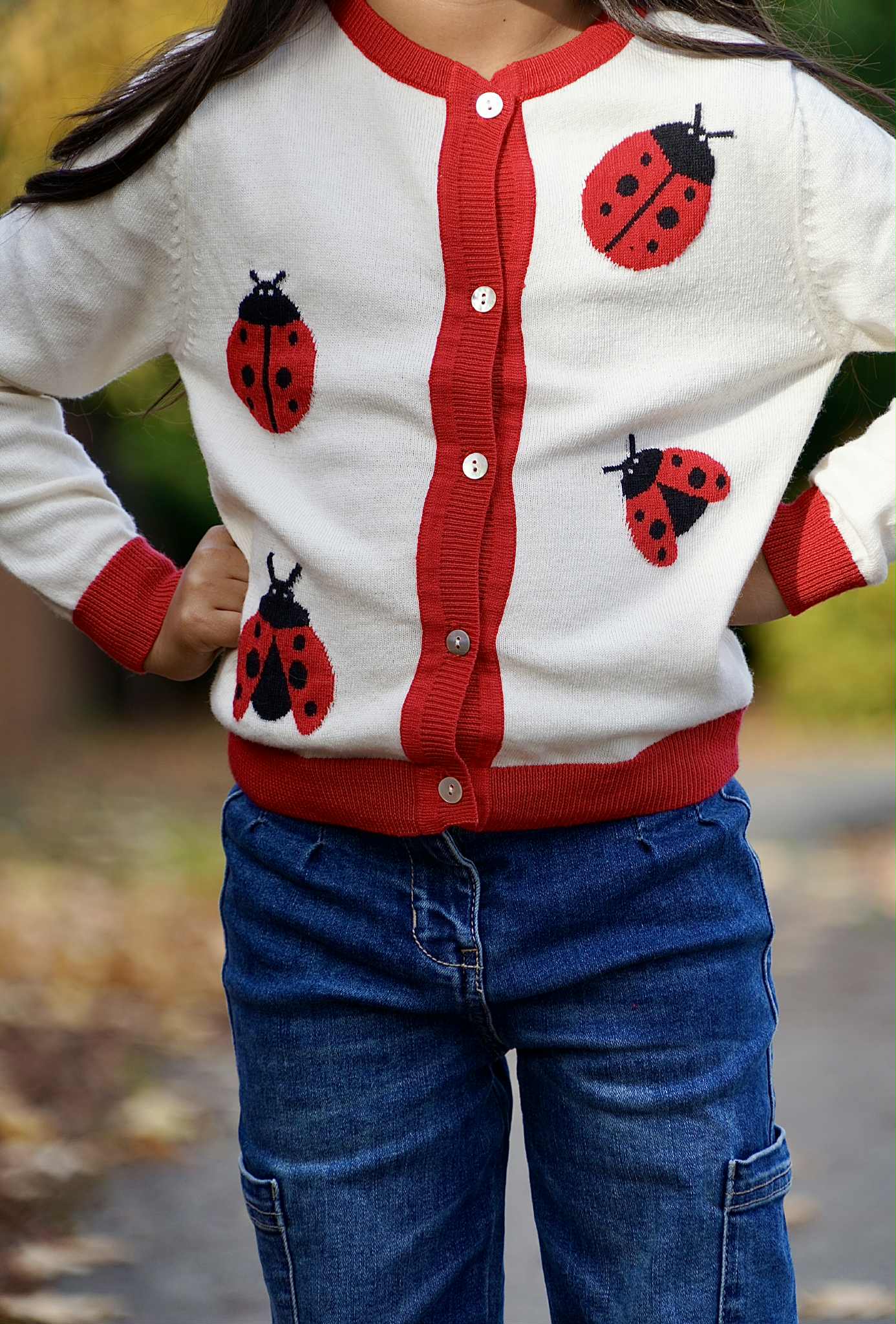 Child wearing a red and white cardigan with ladybug patterns outdoors.