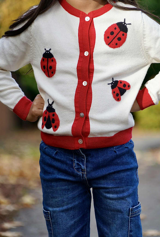 Child wearing a red and white cardigan with ladybug patterns outdoors.