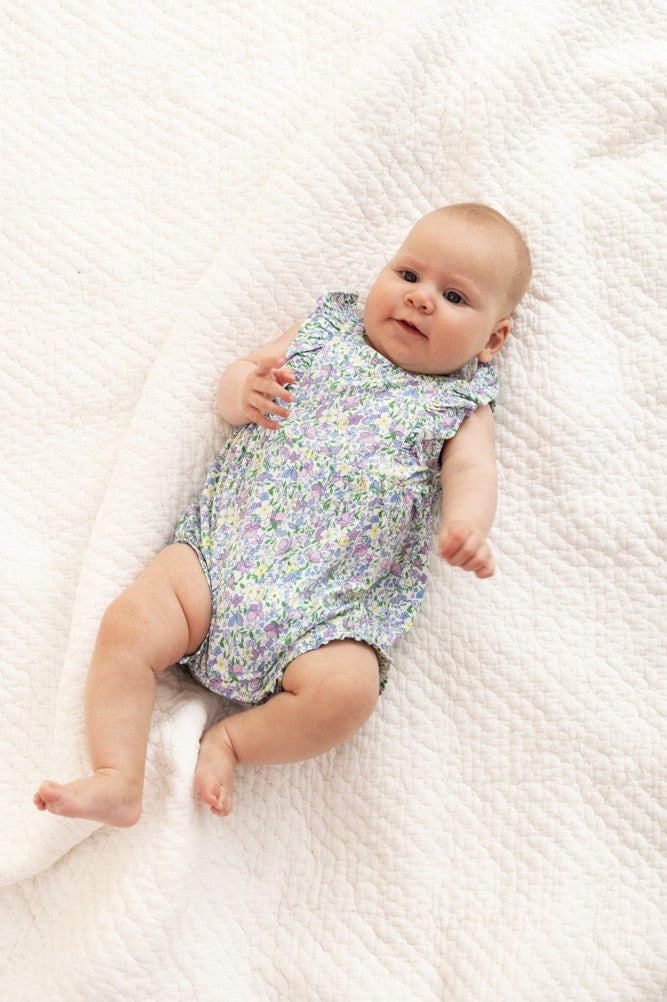 Baby lying on a white textured blanket wearing a floral romper.