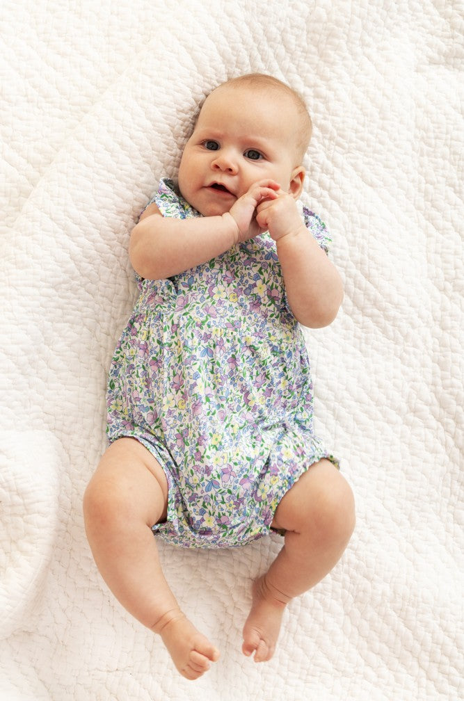 Baby lying on a white textured blanket wearing a floral onesie.