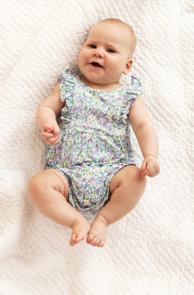 Baby wearing a floral onesie lying on a textured white surface