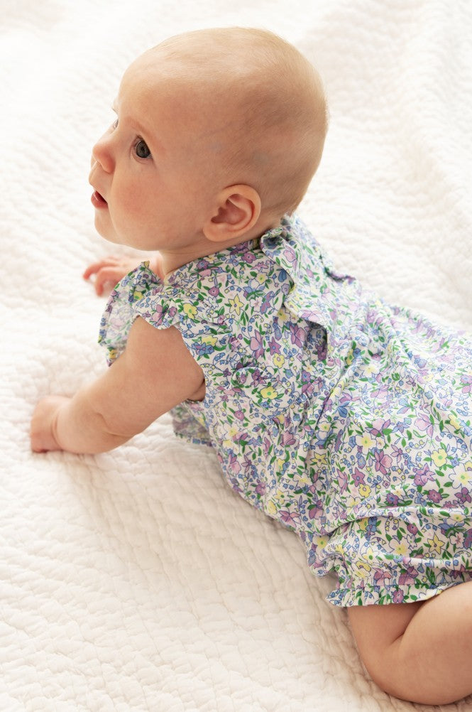 Baby in a floral outfit lying on a white textured surface