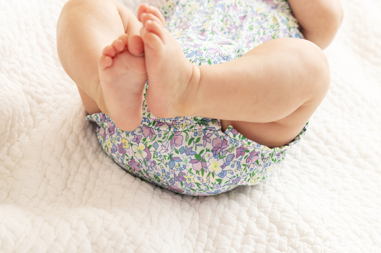 Baby wearing a floral baby romper on a white blanket
