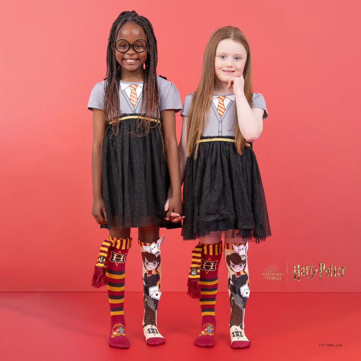 Two children wearing matching outfits with Harry Potter-themed socks on a red background