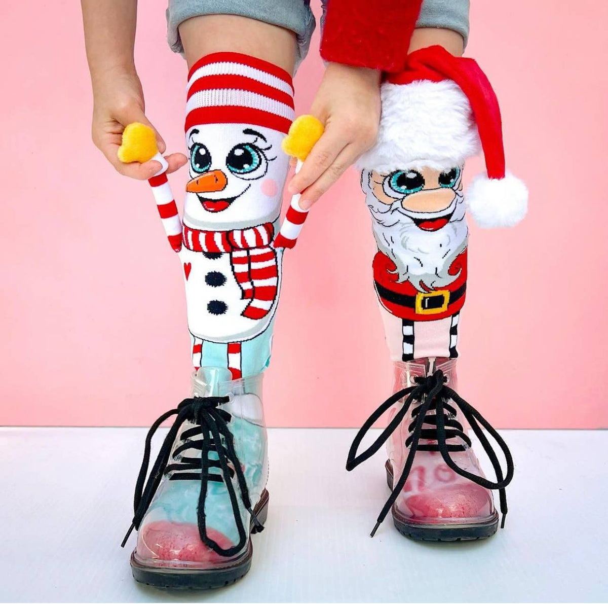 Children's legs wearing socks with snowman and Santa Claus designs against a pink background
