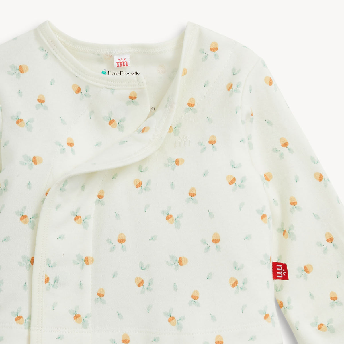 A close-up of a baby long-sleeve wrap blanket or sleep sack in off-white, featuring a delicate all-over print of small acorns and light green leaves. The brand tag 'MM' is visible on the sleeve, and an interior neck label reads 'Eco Friendly'.