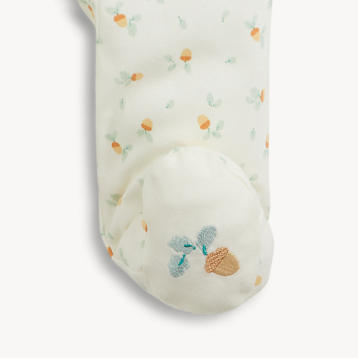 A close-up of a white baby bootie featuring a delicate all-over floral pattern with orange and green accents, and a matching embroidered acorn motif on the toe.
